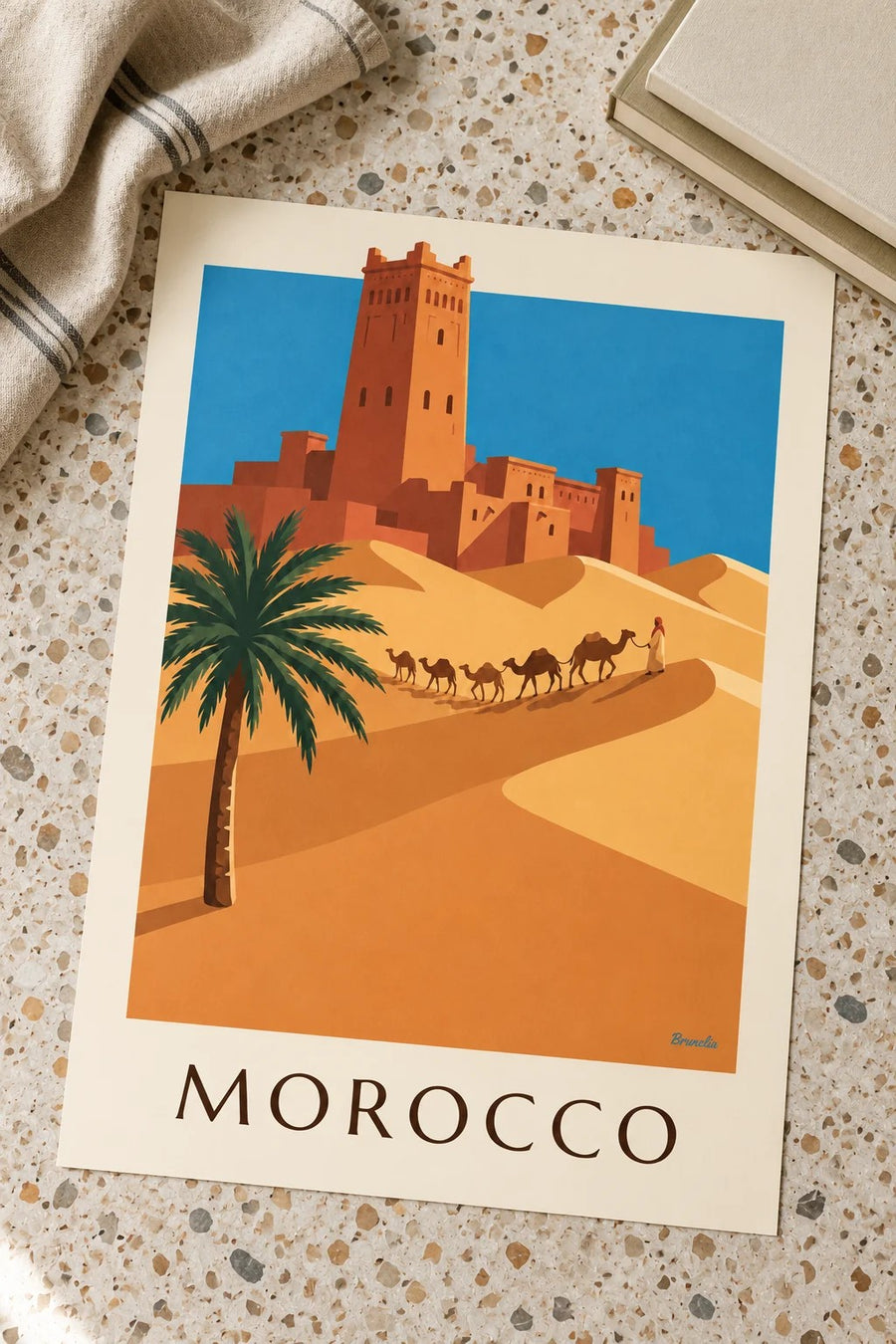 Moroccan desert kasbah and camel caravan poster: placed on a table